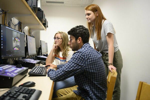 Three undergraduate students looking at screens of video feeds from the child development lab